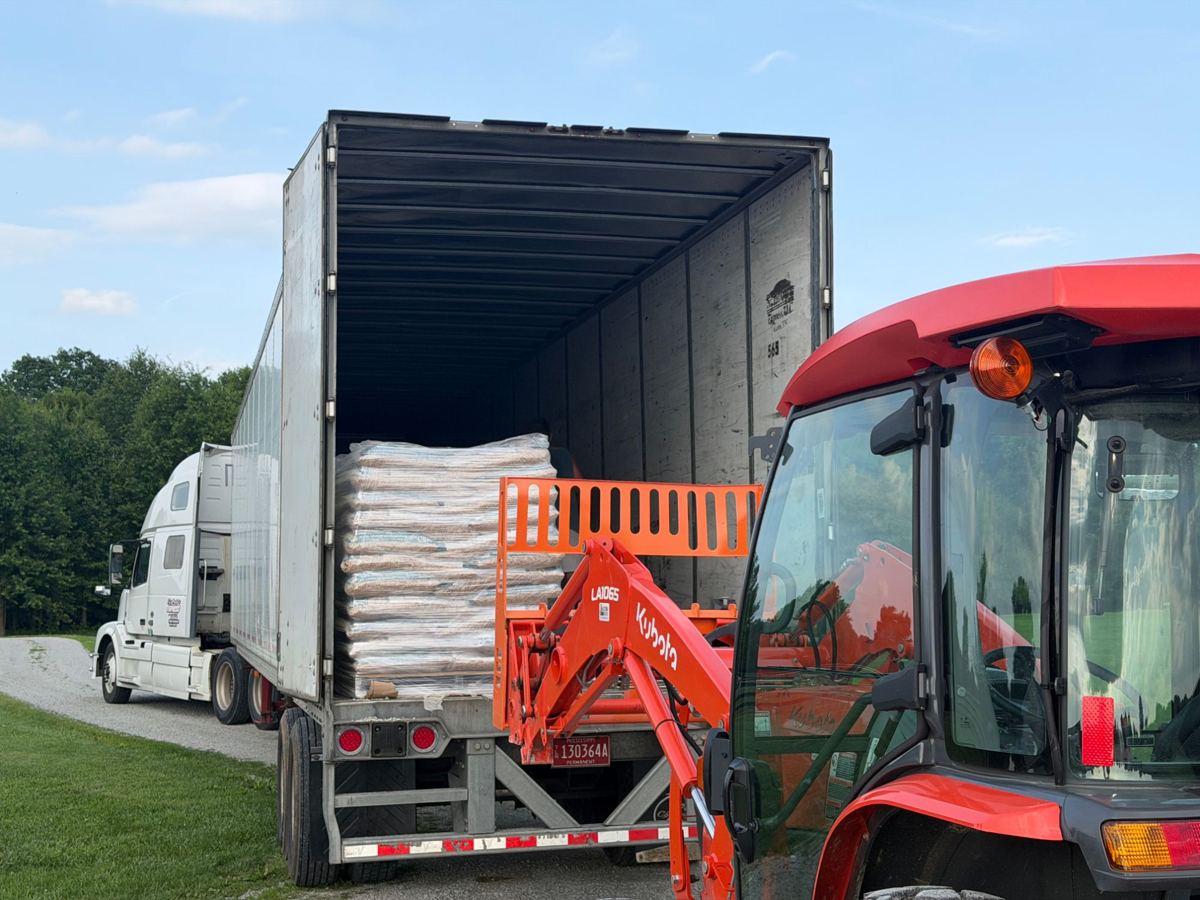 Tractor with pallet forks unloading a pallet of pine pellet bedding from a semi trailer at a horse farm
